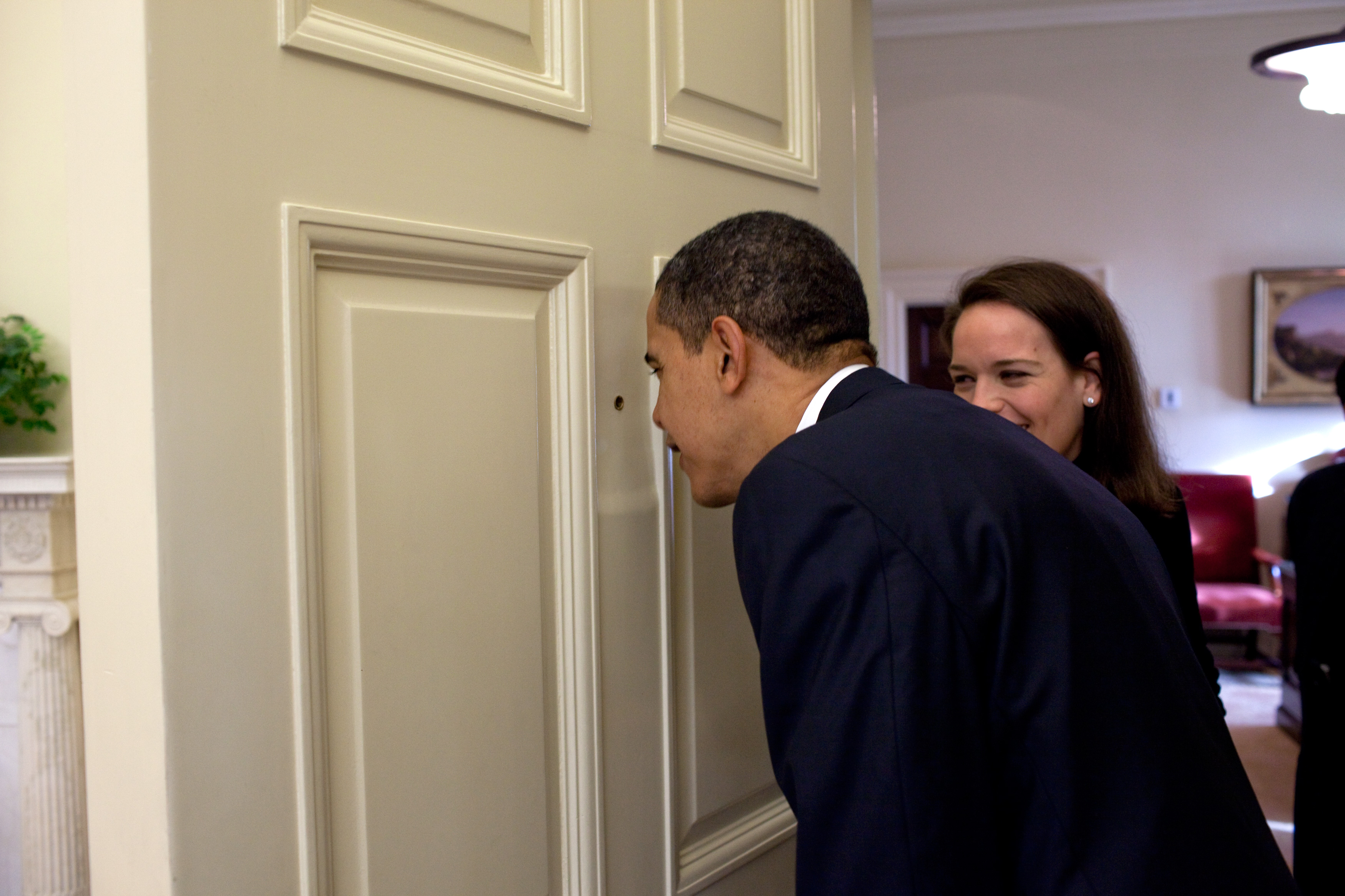 President Barack Obama looks through the Oval Office door peephole as his personal secretary Katie Johnson watches 3/12/09. Official White House Photo by Pete Souza